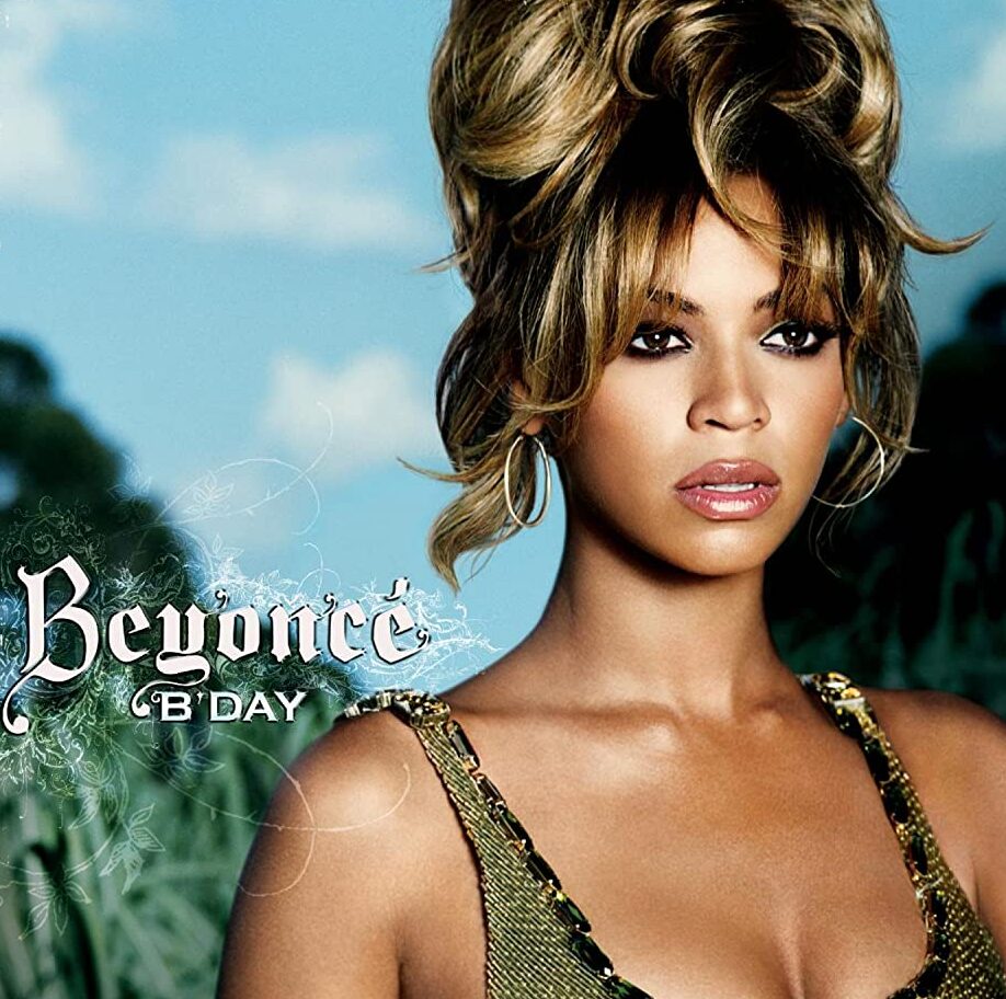 Album cover for Beyonce's "B'Day", which features a portrait angle of Beyonce herself in the center-right. She is standing in front of a marsh, wearing a green sleeveless top and her standard honey-blonde hair in a large bun.